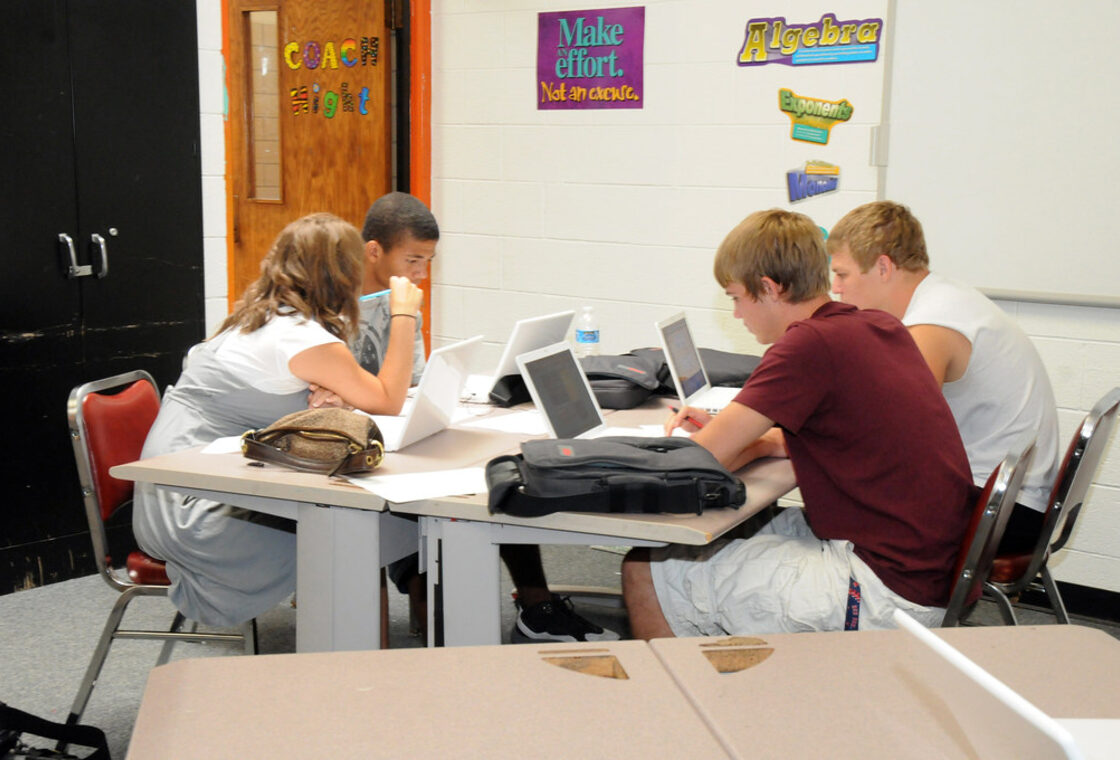 A mentor working through a problem with a young student at a table