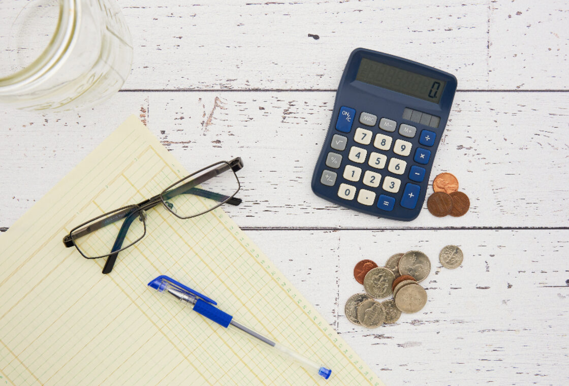 Calculator, coins, glasses and a pen on a desk