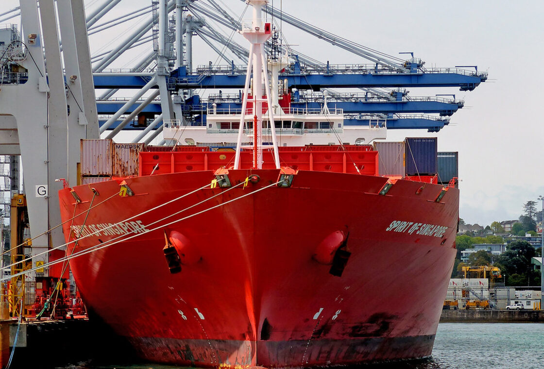 A red container ship docked at a port crane